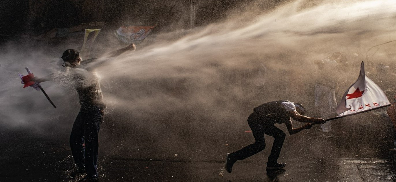 Due ragazzi con una bandiera in mano colpiti da un getto d'acqua.